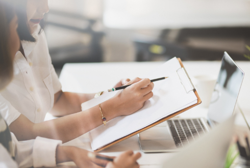 クリップボードを見ながら打ち合わせする女性達の画像
